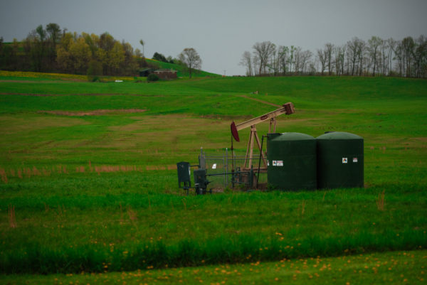 Image of fracking well in the forefront with green rolling hills behind